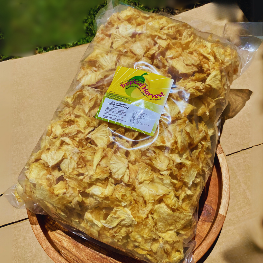 Large 4kg bag of Australian dried pineapple from Tropical Harvest, placed on a wooden board outdoors. The transparent bulk packaging showcases golden yellow dried pineapple pieces, sealed for freshness with a branded label