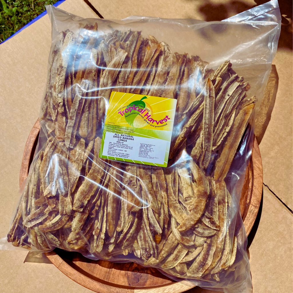 4.5kg bulk pack of Australian dried banana longs in a clear non-resealable bag, labeled with Tropical Harvest branding, displayed on a wooden tray outdoors. Naturally dried with no added sugar or preservatives