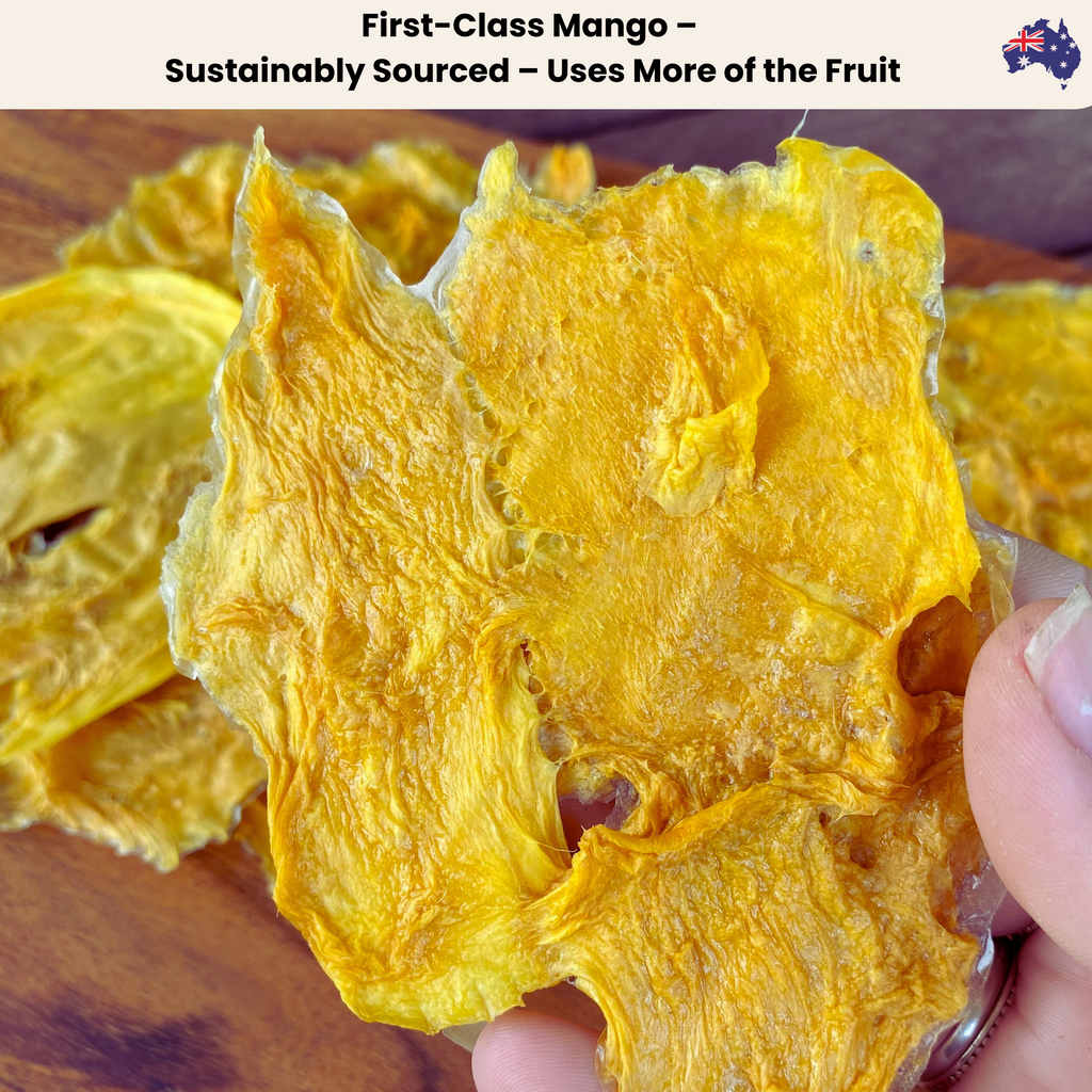 A close-up of a hand holding a sustainably sourced First-Class Australian dried mango slice. The mango piece is golden and slightly irregular in shape, made using more of the fruit to reduce waste while maintaining the naturally sweet, chewy taste.